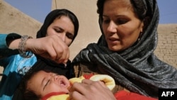 An Afghan woman holds a child as a health worker administers a polio vaccine. Polio-eradication can be dangerous work in some parts of Afghanistan, because some religious extremists have condemned it. 