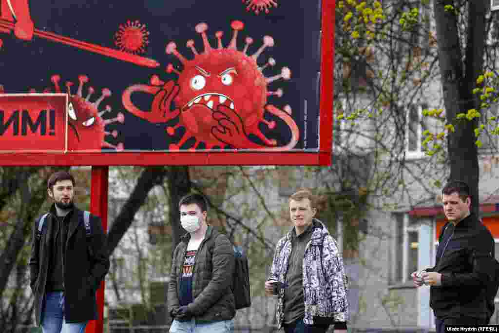 People in Minsk walk past a sign depicting the coronavirus, saying &quot;We will win.&quot;