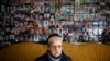 Harja Ćatić sedi ispred zida na kojem su postavljene fotografije žrtava genocida u Srebrenici
