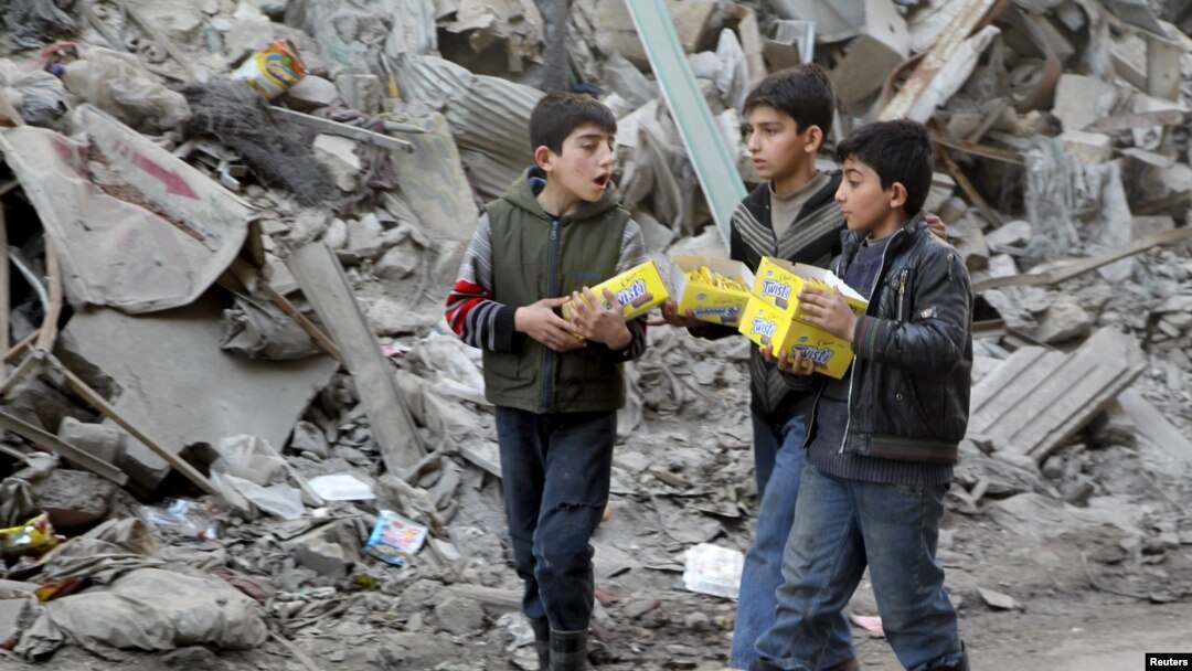 Boys carry boxes of biscuits near rubble of damaged buildings in Aleppo.