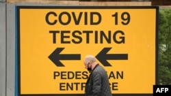 На этом фото пешеход проходит мимо знака, направляющего представителей общественности к центру тестирования на Covid-19 в Болтоне, на северо-западе Англии, 28 мая 2021 года. 