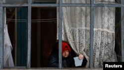 კიევზე რუსული რაკეტებით შეტევის შედეგად დაზიანებული სახლის მცხოვრები ქალი ბინის აივანზე ჩამსხვრეული შუშის ნაწილით. 2026 წლის 12 თებერვალი