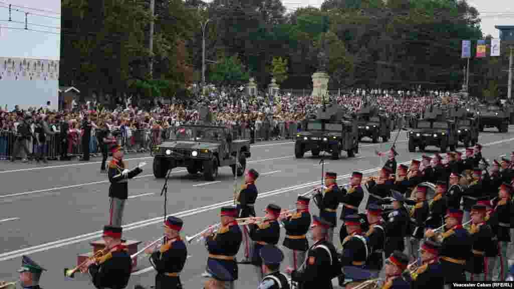 O coloană de vehicule blindate HMMWV trece pe bulevardul Ștefan cel Mare, în timp ce fanfara militară acompaniază defilarea.<br><br>