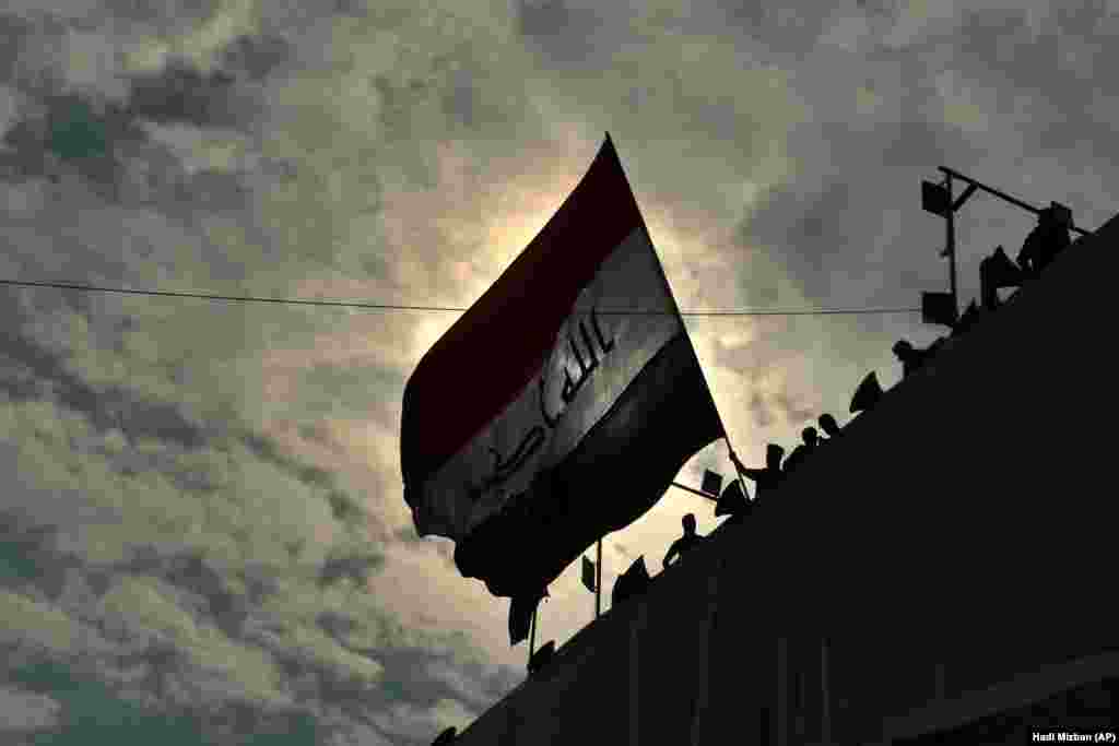 Anti-government protesters wave a flag while standing on a building near Tahrir Square in Baghdad, Iraq. (AP/Hadi Mizban)