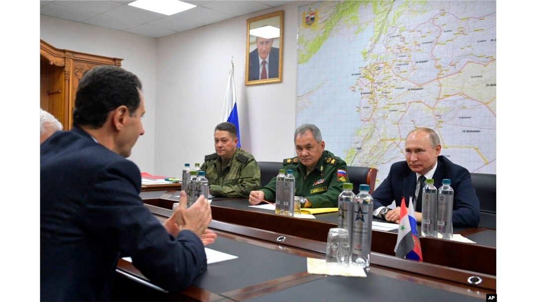 Președintele rus Vladimir Putin (dreapta), secondat de comandanții armatei, îl ascultă pe președintele sirian Bashar Assad la Damasc, în urmă cu aproape cinci ani.