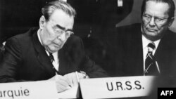 Liderul sovietic Leonid Brejnev semnează pactul final al Conferinței pentru Securitate și Cooperare în Europa, sub privirile liderului iugoslav Iosp Broz, Helsinki, 7 august 1975.