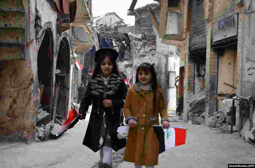 Iraqi girls walk holding their national flag toward a ceremony for the reopening of the Bab al-Saray market in the Old City of Mosul. (AFP/Ahmad Muwafaq)