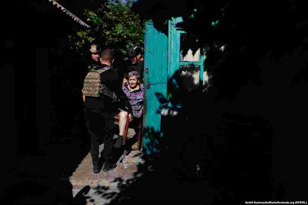 Волонтери Сергій, Даніїл і Оуен із Нової Зеландії виносять жінку з будинку та під звуки віддалених вибухів несуть її до автівки – під час евакуації цивільних з Новогродівки Донецької області, серпень 2024 року.Волонтери продовжують допомагати з евакуацією літніх та маломобільних людей з районів, наближених до лінії фронту