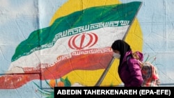 Иранская девушка проходит мимо настенной живописи с изображением национального флага Ирана на улице в Тегеране, Иран, 22 января 2022 года. 