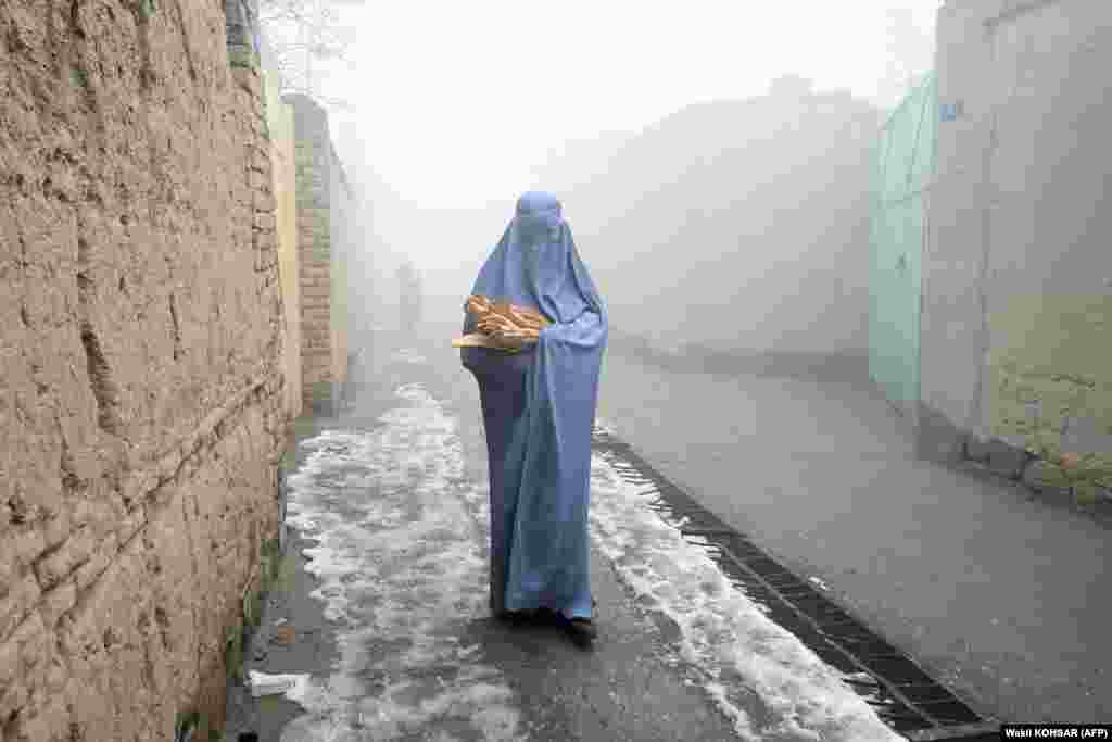 A woman wearing a burqa walks along a road toward her home after receiving free bread from a charity in Kabul.