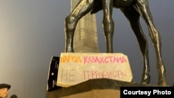 Граждане и плакат «Народ Казахстана не террористы» возле памятника у монумента Независимости в окутанном туманом Алматы. 6 января 2022 года
