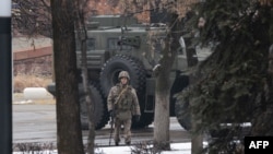 Озброєний співробітник сил безпеки у спецобмундируванні на тлі військової техніки в Алмати, 8 січня 2022 року