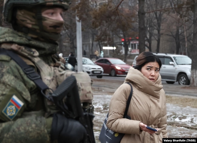 Алматы көшесін бақылап тұрған Ресей қарулы сарбазына қарап өтіп бара жатқан қыз. 11 қаңтар 2022 ж.