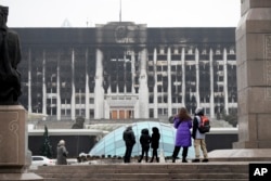 Місцеві жителі дивляться на обгорілу будівлю мерії Алмати, 11 січня 2022 року