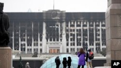 Люди смотрят на здание мэрии на центральной площади, заблокированной казахстанскими войсками и полицией в Алматы, Казахстан, вторник, 11 января 2022 года. 