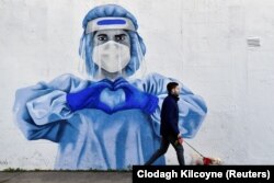Një person pa maskë në Dublin të Irlandës kalon pranë një murali dedikuar punëtorëve shëndetësorë. 12 janar 2022.