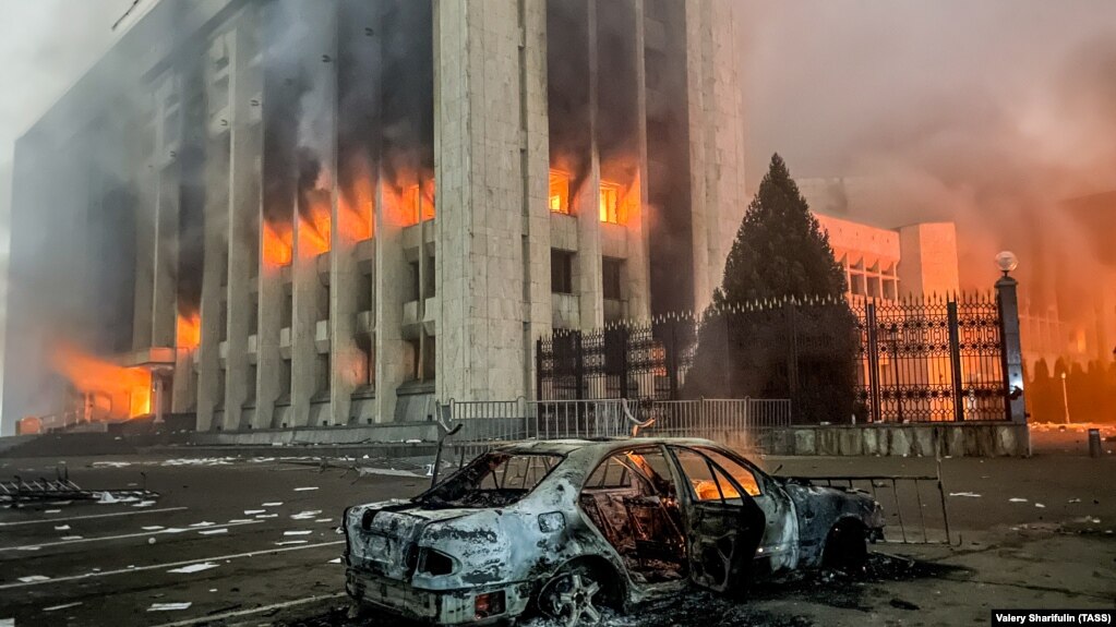 Сожженная машина видна перед горящим зданием акимата. Протесты распространяются по Казахстану из-за роста цен на топливо; протестующие ворвались в акимат Алматы и подожгли его