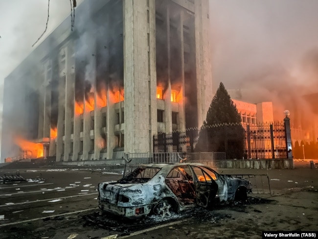 Сгоревший автомобиль возле горящего здания акимата Алматы. Участники протеста против роста цен на топливо ворвались в здание акимата и подожгли его