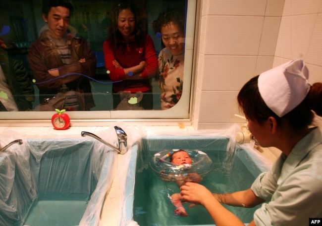 Члены китайской семьи смотрят, как медсестра купает родившегося у одной из их родственниц младенца