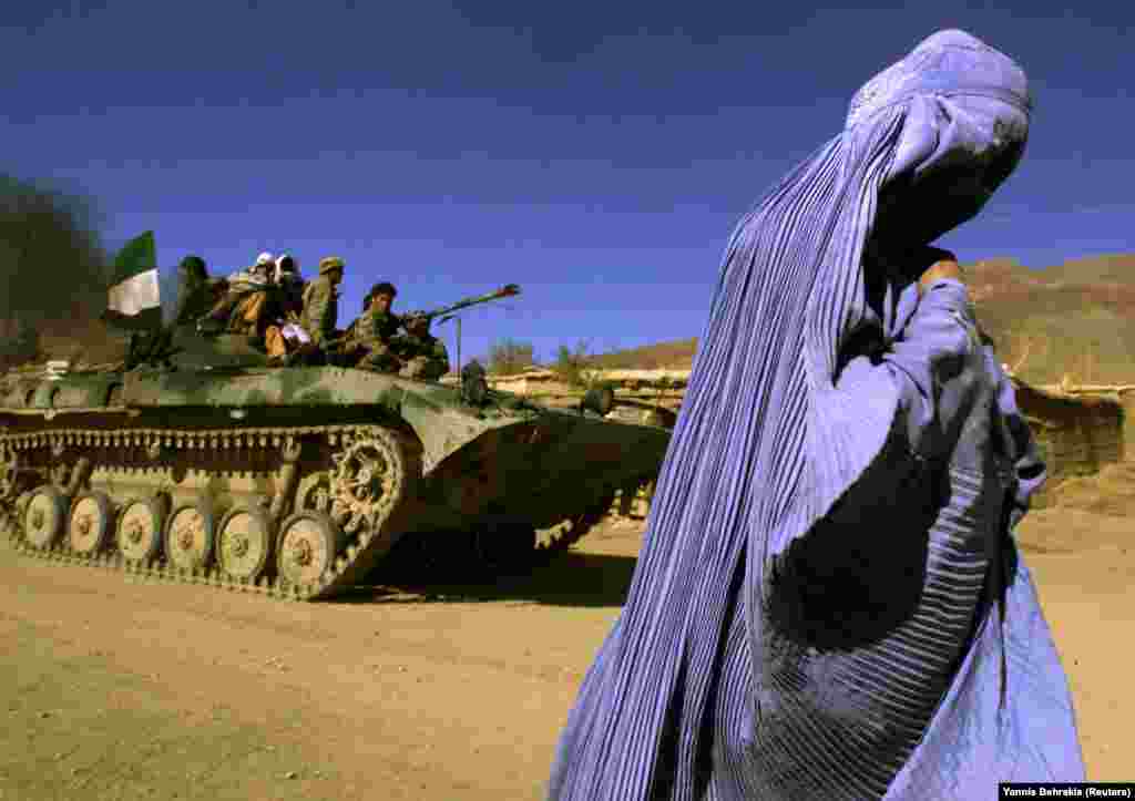 Авганистанка со бурка оди по улица, додека зад неа поминува тенк со борци што го развиорија знамето на Авганистан. (Џабал Сарај, 4 ноември 2001 година)
