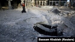 A Syrian woman walks past damaged buildings in Douma, in the eastern Damascus suburb of Ghouta, on November 15.