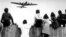 GERMANY -- An undated file photo shows Berlin children sitting on a fence of the Tempelhof airport watching a so called 'Raisin Bomber' approaching for landing. 