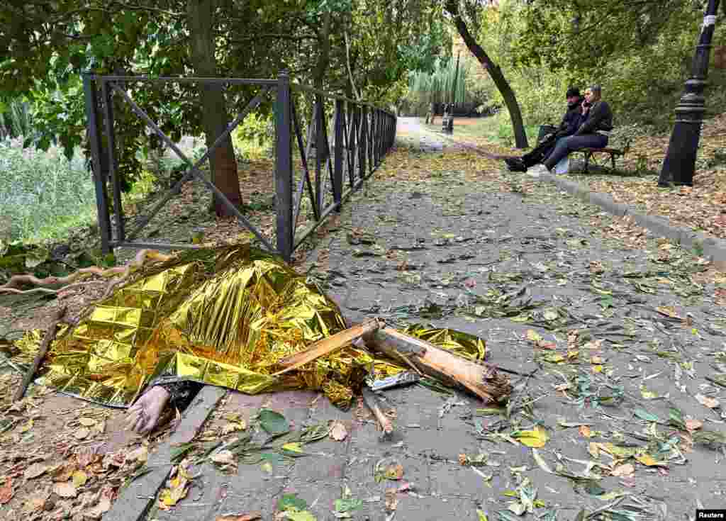 Locals sit on a bench near the body of a woman killed during a Russian air strike in Kharkiv.