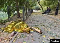 Local residents sit on a bench at a lakeshore in Kharkiv earlier this month as the body of a woman killed during a Russian air strike lies nearby. The crisis in the Middle East is drawing the world's attention away from Ukraine, where Moscow's forces are killing civilians on an almost daily basis.