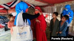 A UNICEF worker helps an internally displaced girl put on a face mask at a makeshift camp in Jalalabad. According to a new report by Amnesty International, IDPs in Afghanistan are living in conditions that are "perfectly suited" to the rapid transmission of the coronavirus. 