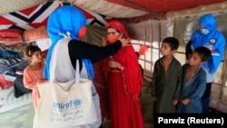 A UNICEF worker helps an internally displaced girl put on a face mask at a makeshift camp in Jalalabad. According to a new report by Amnesty International, IDPs in Afghanistan are living in conditions that are "perfectly suited" to the rapid transmission of the coronavirus. 
