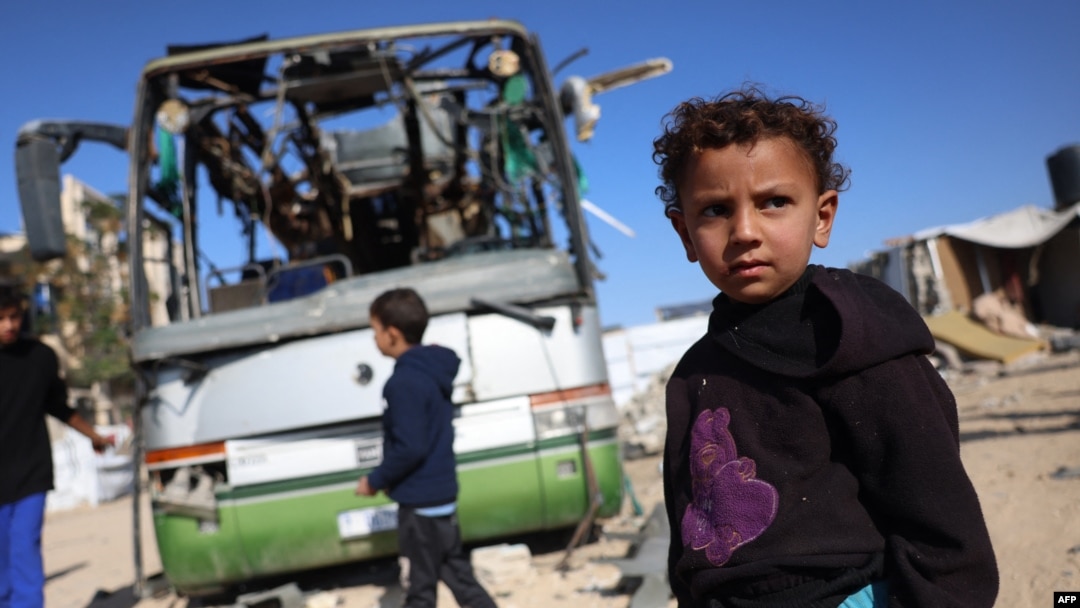 Mai mulți copii se uită la carcasa unui autobuz distrus de un atac israelian în zona Mawasi, la vest de orașul Khan Yunis, în sudul Fâșiei Gaza, pe 23 decembrie 2024.