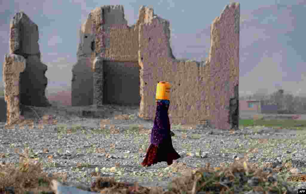 An Afghan woman carries a water canister past the ruins of a building destroyed during the Afghan-Soviet war on the outskirts of Jalalabad in Nangarhar Province. (AFP/Noorullah Shirzada)