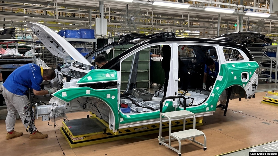 Angajați care lucrează la un vehicul electric (EV) de pe o linie de producție a unei fabrici care aparține Jiangling Group Electric Vehicle in Nanchang, provicia Jiangxi, China.