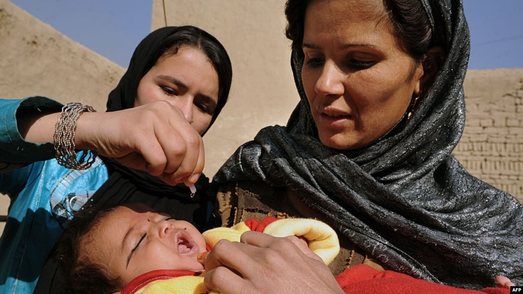 An Afghan woman holds a child as a health worker administers a polio vaccine. Polio-eradication can be dangerous work in some parts of Afghanistan, because some religious extremists have condemned it. 