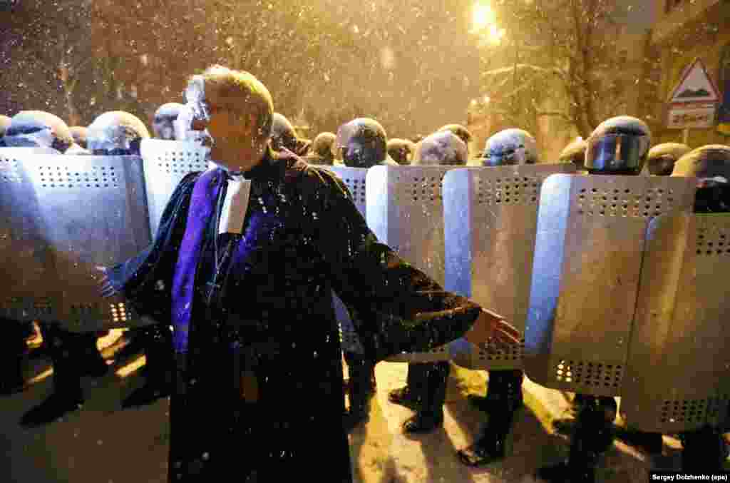 A priest speaks to protesters in front of a police line.