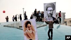 Dy djem duke mbajtur fotografitë e liderit suprem Ayatollah Ali Khamenei, në të djathtë, dhe themeluesit të Republikës Islamik Ayatollah Khomeini, majtas, gjatë marsheve të mbajtura në Teheran më 11 shkurt.
