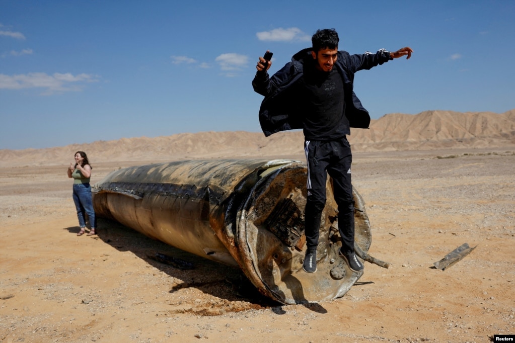 A man jumps off the apparent remains of a ballistic missile lying in the desert, following an attack by Iran on Israel, near the southern city of Arad, Israel, on October 2.