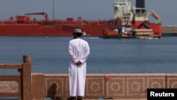 A man stands near the waterfront as a vessel sits at anchor at Sultan Qaboos Port in Muscat, Oman.