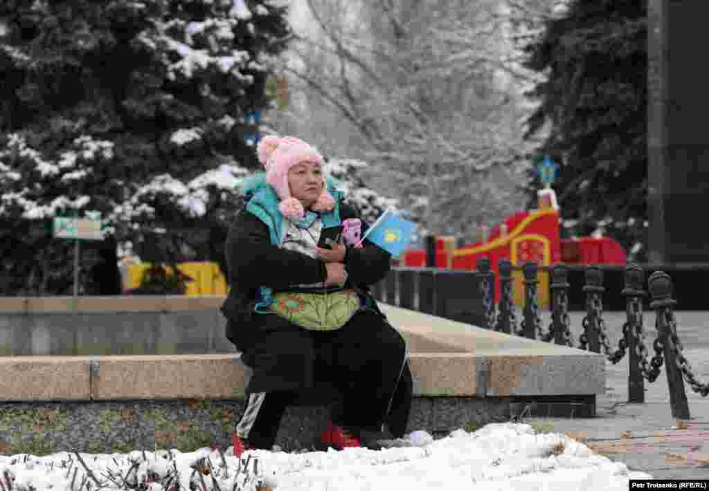 Женщина с флажком Казахстана сидит неподалеку от места, где проходит митинг.