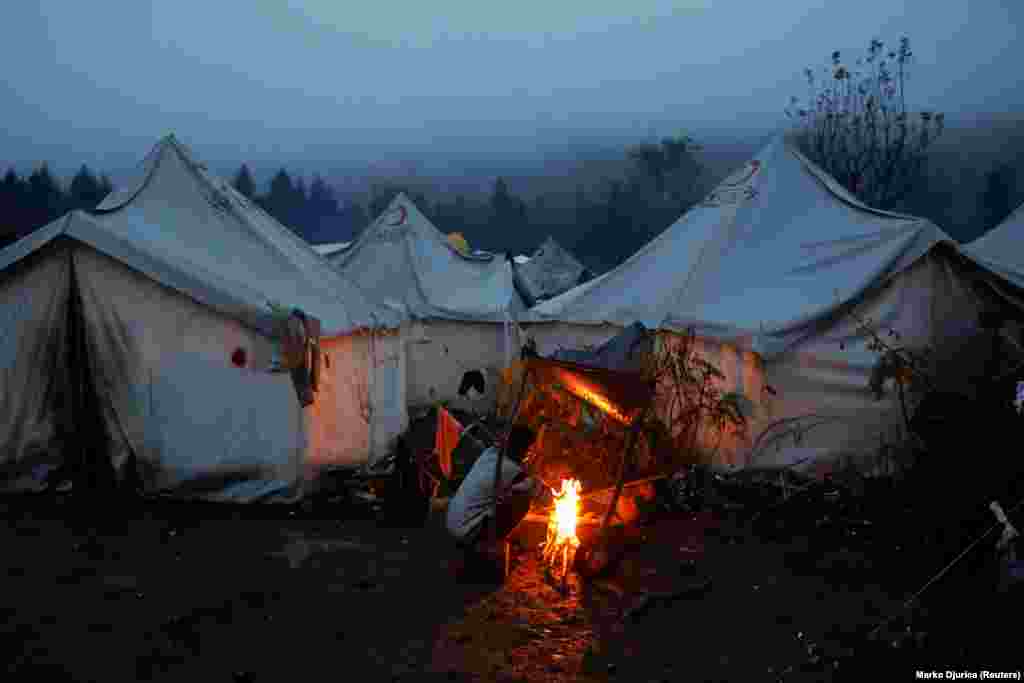 A migrant huddles next to a fire as cold weather begins to bite in the makeshift camp, a few kilometers from the border with Croatia.