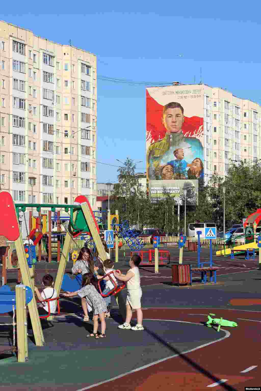 Djeca se igraju na igralištu u Nadimu, na sjeveru Rusije, u junu 2025. godine.U pozadini se vidi bilbord koji reklamira vojne ugovore i mural posvećen tinejdžeru, vojniku Crvene armije, koji je poginuo 1944. godine boreći se protiv nacističkih snaga u današnjoj Bjelorusiji.