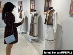 O femeie din Iași admiră câteva dintre costumele tradiționale din colecția Marius Matei. Iunie 2025.