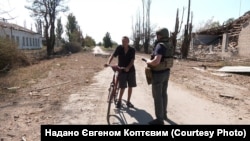 Євген Коптєв та місцевий житель під час евакуації з села Романки Дніпропетровської області. Позаду видно зруйновану будівлю через атаку КАБами