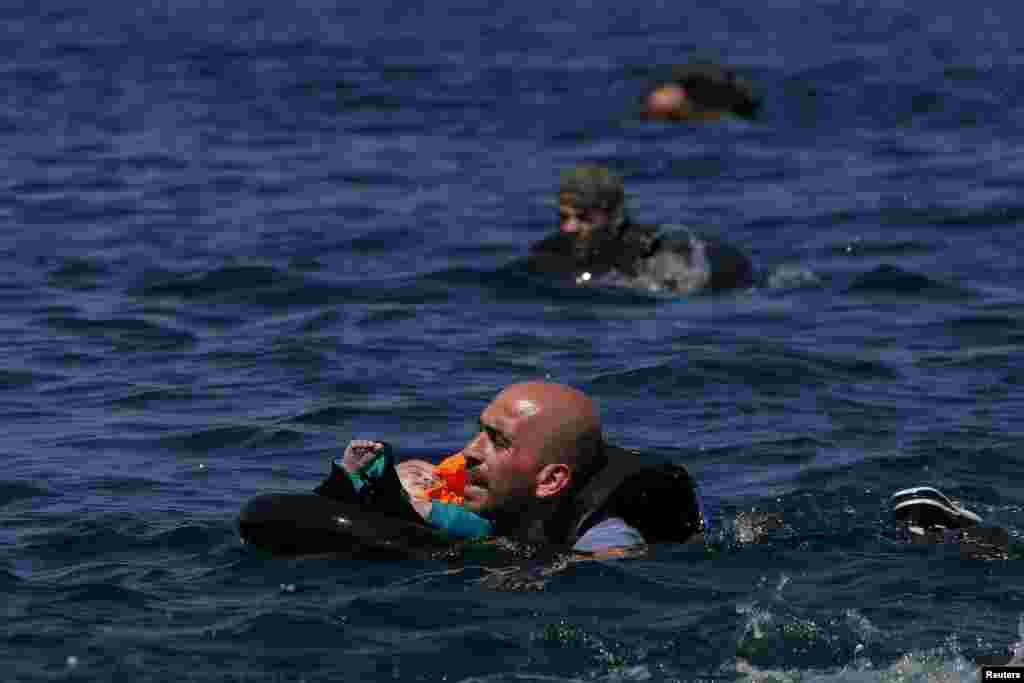 A Syrian refugee holding a baby in a lifetube swims toward shore after their dinghy deflated some 100 meters offshore of the Greek island of Lesbos. (Reuters/Alkis Konstantinidis)