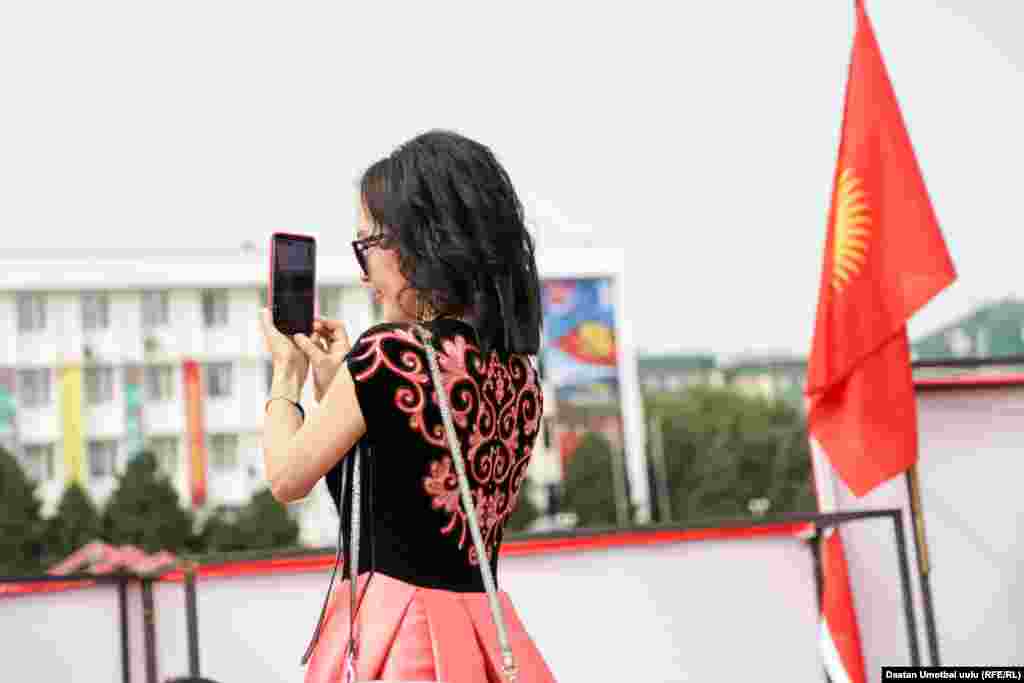 A woman in a dress with traditional embroidery photographs festivities in Osh.