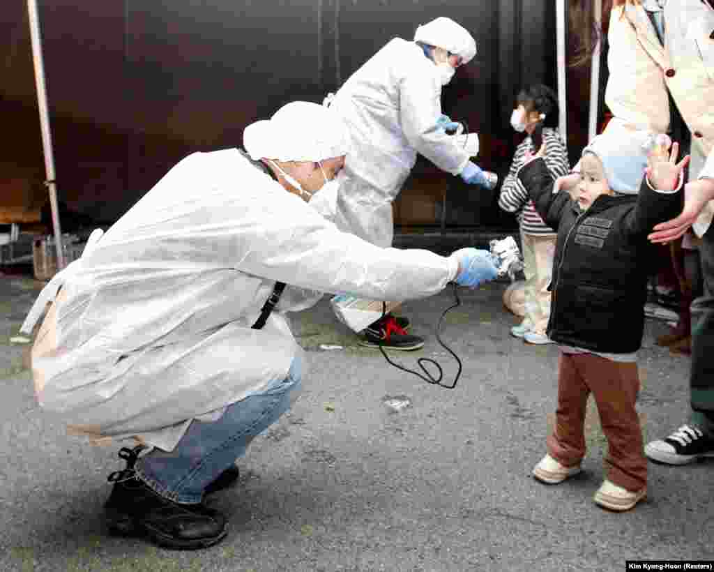 Zyrtarët, të veshur me rroba mbrojtëse,&nbsp;kontrollojnë fëmijët për rrezatim. Këta fëmijë u evakuuan nga Koriyama, që gjendet në afërsi të centralit në Fukushima. Japoni, 13 mars, 2011.&nbsp;