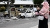 یک زن محجبه از خودروهایی که در اعتراضات فرانسه آتش گرفته‌اند عکس می‌گیرد؛ پنجشنبه هشتم تیر، حومه پاریس