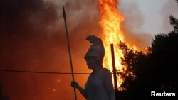 Statuie antică având ca fundal un incendiu în apropiere de Atena. 