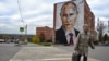 RUSSIA -- An elderly woman crosses a road in front a mural painting depicting Russian President Vladimir Putin, on the wall of a house, in the town of Kashira, some 115 km southeast of Moscow, October 16, 2017