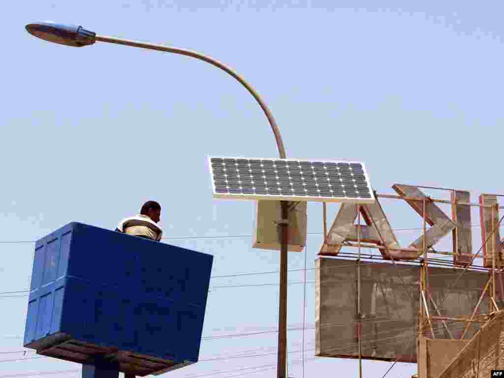 Iraq -- A municipal worker is lowered after adjusting a solar panel attached to the top of an electricity pylon along the central isle of a main road in the Karada district of Baghdad, 24May2008 - IRAQ, Baghdad : A municipal worker is lowered after adjusting a solar panel attached to the top of an electricity pylon along the central isle of a main road in the Karada district of Baghdad on May 24 2008.The solar panel which are made in China are set to fill sun power during day light hours and run the streets lights at night. The Ministry of Electricity plans on using solar power to light the main Baghdad ring road and airport highway at night. AFP PHOTO / SABAH ARAR green03 Replacing fossil fuels with renewable energy for electricity